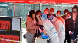 Petugas medis mengambil sampel warga saat yang lainnya antre untuk tes COVID-19 di dekat daerah perumahan di Qingdao, China, Senin (12/10/2020). Lebih dari 9 juta orang yang tinggal di kota Qingdao, menjalani tes virus Corona (COVID-19) secara massal setelah muncul kasus baru. (Chinatopix via AP)