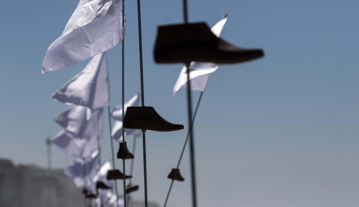 Sejumlah cetakan kayu sepatu dengan bendera putih yang merupakan seni instalasi di pajang di Playas de Tijuana, Meksiko (7/10). Seni instalasi yang bercerita tentang migran Meksiko ini adalah karya seniman Betsabee Romero. (AFP Photo/Guillermo Arias)