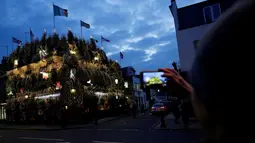 Pejalan kaki mengambil gambar dari bangunan bar The Churchill Arms yang ditutupi pohon natal dan lampu warna-warni di London, Inggris, 20 Desember 2016. Churchill Arms memang dikenal berkat dekorasi Natalnya yang sangat meriah. (REUTERS/Neil Hall)