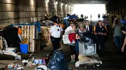 Sepasang wanita dan pria yang tinggal di bawah jembatan membawa barang mereka usai diusir petugas di Philadelphia (30/5). Para tunawisma ini diusir karena tempat mereka tinggal biasa digunakan untuk mengkonsumsi heroin. (AP Photo/Matt Rourke)