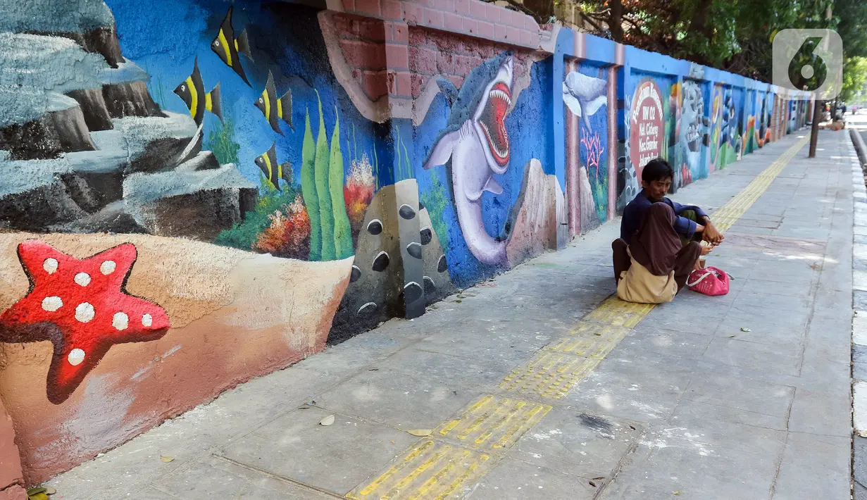 Warga duduk di trotoar dekat mural bertema biota laut yang menghiasi dinding di kawasan Cideng, Jakarta, Rabu (29/11/2023). Mural dibuat guna memperindah sekaligus penataan kawasan Kelurahan Cideng, Jakarta Pusat. (Liputan6.com/Herman Zakharia)