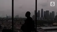 Seseorang melintas dekat jendela berlatar gedung bertingkat dan permukiman di kawasan Jakarta, Senin (17/1/2022). Bank Dunia memproyeksikan pertumbuhan ekonomi Indonesia pada tahun 2022 mencapai 5,2 persen. (Liputan6.com/Angga Yuniar)