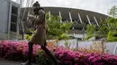 Seorang wanita berjalan di luar Stadion Nasional Jepang, tempat upacara pembukaan dan penutupan untuk Olimpiade Tokyo 2020 akan diadakan, saat bunga azalea bermekaran di Tokyo (6/4/2021). Ibukota Jepang mengonfirmasi lebih dari 390 kasus virus korona baru pada hari Selasa. (AP Photo/Kiichiro Sato)