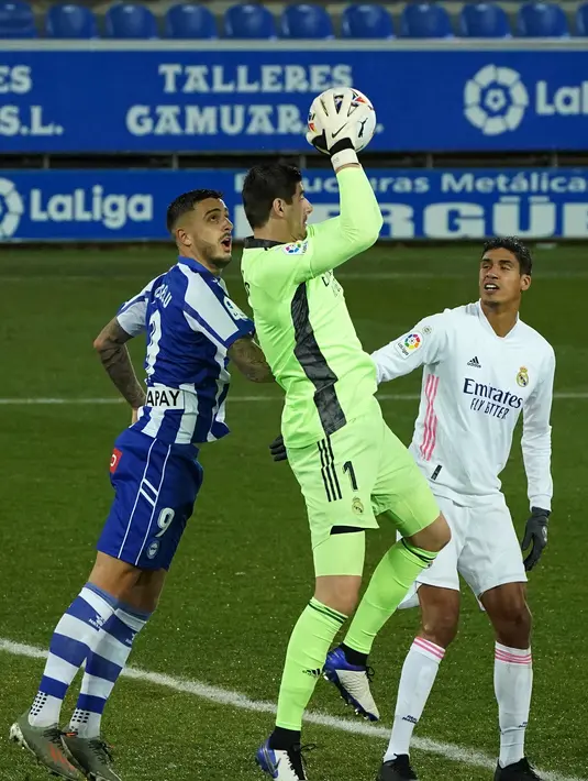 Kiper Belgia Real Madrid Thibaut Courtois melompat untuk melakukan penyelamatan selama pertandingan melawan Deportivo Alaves di stadion Mendizorroza di Vitoria. Minggu (24/1/2021). Alaves terpuruk di posisi ke-17 dengan nilai 18. Mereka hanya satu poin dari zona degradasi. (AFP/ Cesar Manso)