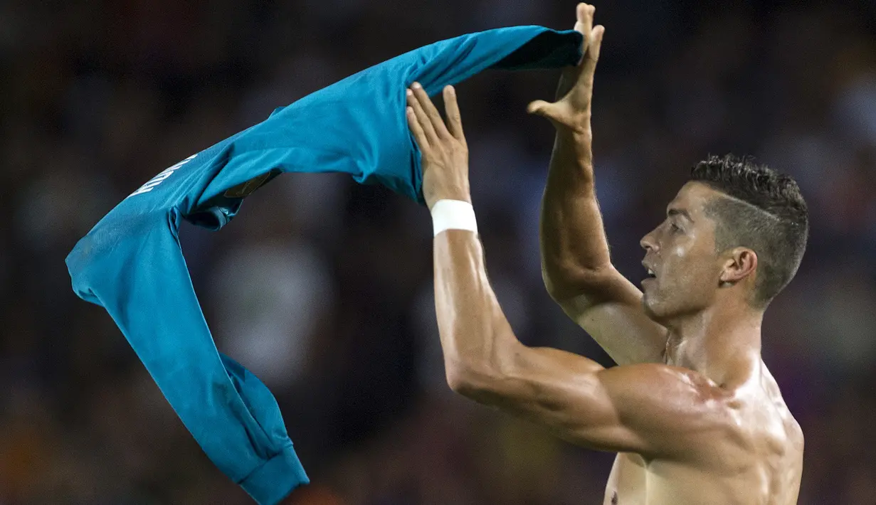 Pemain Real Madrid, Cristiano Ronaldo mengangkat jerseynya tinggi-tinggi di hadapan suporter Camp Nou pada leg pertama Piala Super Spanyol, Senin (14/8). Aksi selebrasi Ronaldo ini serupa yang dilakukan Lionel Messi sekitar April lalu. (STRINGER/AFP)
