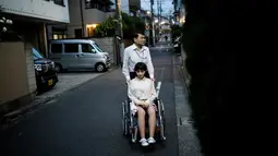 Masayuki Ozaki berjalan bersama boneka seksnya yang berada di kursi roda di Tokyo, Jepang (9/6). Ozaki mengaku, ia merasa jatuh cinta pada pandangan pertama saat melihat Mayu di ruang pameran. (AFP photo/Benrouz Mehri)