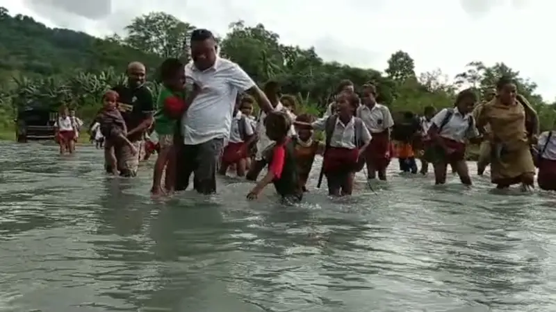 Puluhan siswa dibantu kepala desa, aparat desa dan guru saat menyebrangi sungai.(Liputan6.com/Dionisius Wilibardus)