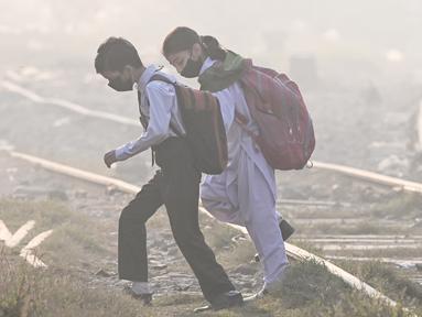 Anak-anak sekolah mengenakan masker berjalan melintasi rel kereta api di tengah kabut asap tebal di Lahore, Pakistan pada Rabu 20 November 2024. (Arif ALI/AFP)