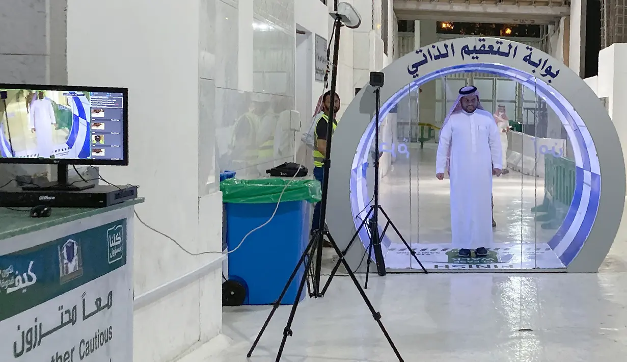 Seorang pria melewati gerbang sterilisasi mandiri yang didirikan di pintu masuk Ka'bah dan Masjid Haram selama bulan suci Ramadan di Mekkah pada 8 Mei 2020. Gerbang ini dipasang sebagai bagian dari tindakan pencegahan yang telah dilakukan sejak pecahnya Pandemi virus Corona (COVID-19). (STR / AFP)