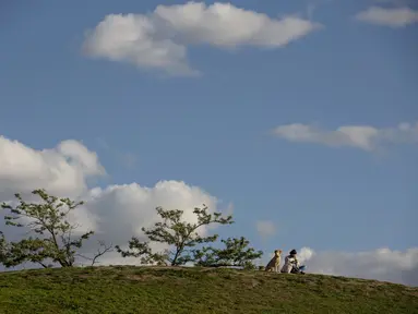 Seorang wanita duduk dengan anjingnya di taman Cerro del Tio Pio di Madrid, Spanyol (14/10/2020). Berbagai wilayah di Spanyol, termasuk Navarra utara dan timur laut Catalonia, sedang merencanakan atau menerapkan pembatasan baru terhadap penyebaran virus corona baru. (AP Photo/Manu Fernandez)