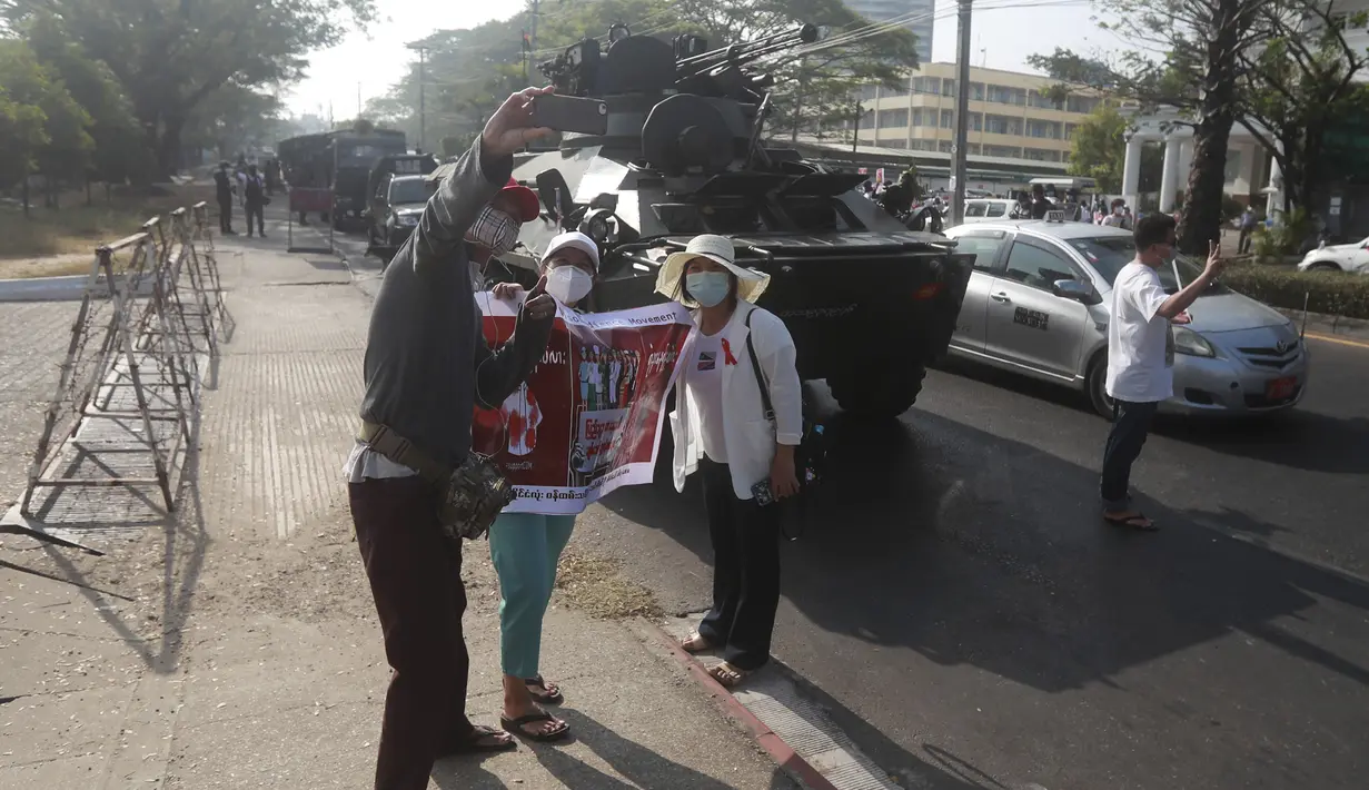 Pengunjuk rasa anti-kudeta berswafoto di depan kendaraan lapis baja yang dikerahkan di luar gedung Bank Sentral Myanmar di Yangon, Senin (15/2/2021). Pasukan militer Myanmar mulai menerjunkan kendaraan lapis baja di kota-kota besar di Myanmar dan memutus akses internet. (AP Photo)