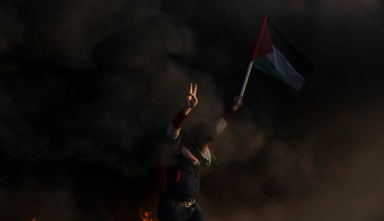 Warga Palestina membakar ban dan mengibarkan bendera nasional saat protes terhadap serangan militer Israel terhadap kamp pengungsi Jenin di perbatasan Israel-Palestina, sebelah timur Kota Gaza, 26 Januari 2023. Dalam serangan Israel ke kamp pengungsi di Jenin, yang oleh warga Palestina disebut pembantaian, setidaknya 20 orang dilaporkan terluka akibat peluru tajam. Empat di antaranya dalam kondisi kritis. (AP Photo/Fatima Shbair)