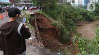 Warga melihat Lokasi longsor di daerah bantaran sungai Ciliwung, Pengadegan Timur, Jakarta, Selasa (12/4/2022). Longsor sepanjang 25 meter, lebar lima meter, dan kedalaman 15 meter itu menyebabkan 4 sepeda motor tertimbun material longsor, namun tidak ada korban jiwa. (Liputan6.com/Herman Zakharia)