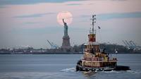 Bulan purnama terlihat di belakang Patung Liberty, New York City, Amerika Serikat, Kamis (7/5/2020). Fenomena supermoon atau di belahan Bumi lain disebut flower moon ini merupakan yang terakhir di tahun 2020. (Johannes EISELE/AFP)