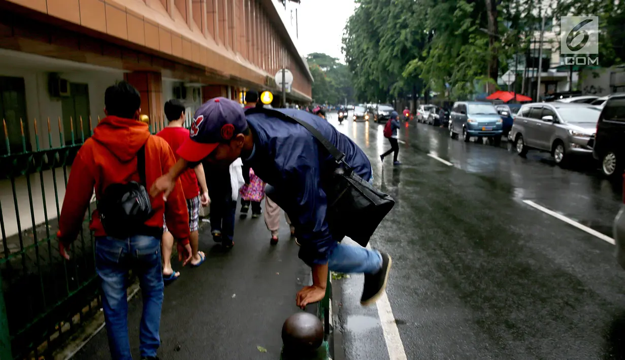 Seorang pria memanjat pagar pembatas di Stasiun Cikini, Jakarta, Rabu, (20/12). Banyaknya penumpang yang mencari jalan pintas dengan melompat pagar untuk menuju akses pintu keluar menyebabkan kemacetan di kawasan stasiun. (Liputan6.com/Johan Tallo)