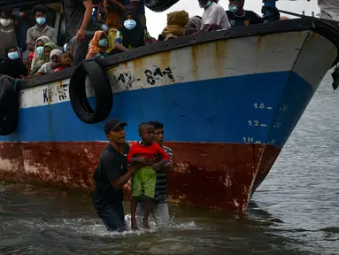 Nelayan Aceh membantu evakuasi seorang anak pengungsi etnis Rohingya menuju pesisir pantai desa Lancok, di Kabupaten Aceh Utara, Kamis (25/6/2020). Hampir 100 orang etnis Rohingya, termasuk 30 orang anak-anak ditemukan terdampar di tengah laut dengan kondisi kapal rusak. (CHAIDEER MAHYUDDIN/AFP)