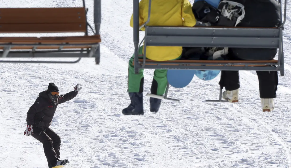 Pemain snowboard menuruni lereng saat dua orang lainnya duduk di kursi gantung di resor ski Tochal di kota Teheran, Iran (1/1/2022). Di tengah polusi udara dan kesengsaraan ekonomi, penduduk Teheran menemukan kenyamanan di resor ski di utara Teheran di pegunungan Alborz. (AP Photo/Vahid Salemi)