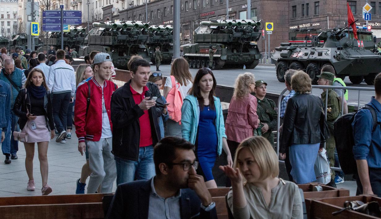 Warga berjalan dengan latar belakang kendaraan militer Rusia yang memenuhi jalanan saat melakukan latihan di Moskow, Rusia (3/5). Pawai akan berlangsung pada 9 Mei di Lapangan Merah Moskow. (AP Photo / Pavel Golovkin)