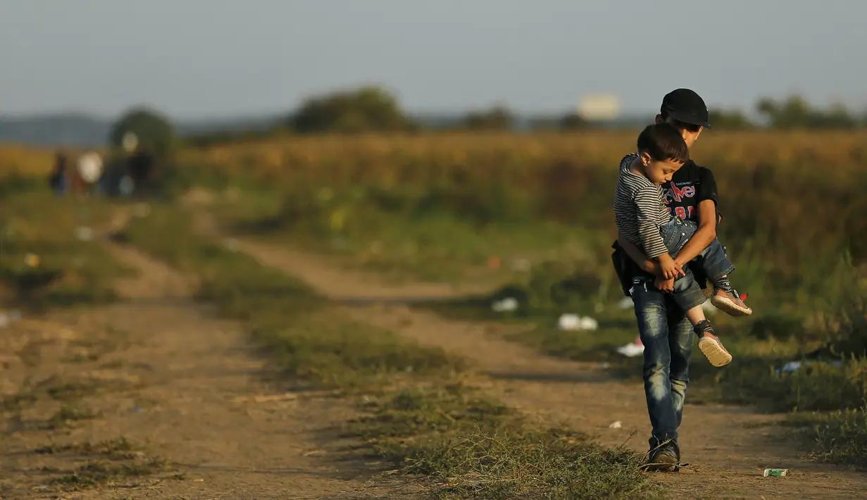 Seorang imigran remaja menggendong adiknya melintasi perbatasan dari Serbia ke Kroasia di Tovarnik (18/9/2015). (REUTERS / Antonio Bronic)