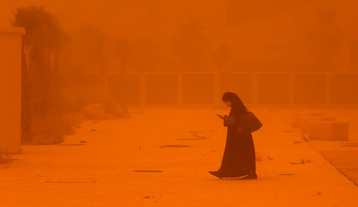 <p>Seorang perempuan melihat-lihat telepon saat berjalan di tengah badai debu yang parah di Kota Kuwait pada 23 Mei 2022. Kabut oranye tebal telah menyelimuti Kuwait pada hari Senin, menyebabkan penerbangan ke dan dari bandara internasional negara itu ditangguhkan sementara, kata regulator penerbangan sipil. (Yasser Al-Zayyat / AFP)</p>