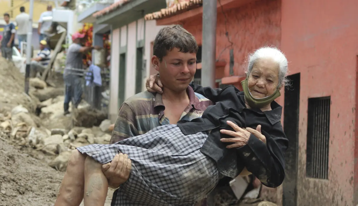 Seorang warga membawa perempuan lansia di jalan yang rusak akibat banjir dan tanah longsor yang dipicu hujan lebat di Tovar, negara bagian Merida, Venezuela, Kamis (26/8/2021). Sedikitnya 20 orang tewas akibat hujan lebat banjir yang terjadi pada Rabu, 25 Agustus. (AP Photo/Luis Bustos)