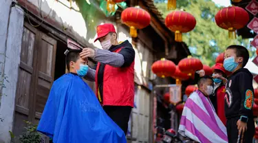 Seorang barber sukarelawan memotong rambut seorang anak laki-laki di sebuah permukiman di Kota Chongqing, China, pada 16 Februari 2020. Sejak merebaknya virus corona COVID-19, sebagian besar tempat potong rambut telah ditutup. (Xinhua/Liu Chan)