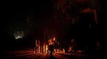 Orang-orang duduk di dekat api unggun menanti kabar kerabat mereka di dekat reruntuhan bangunan yang runtuh di Hatay, Turki, Senin (13/2/2023). Seminggu setelah gempa bumi meluluhlantakkan sebagian wilayah Turki dan Suriah jumlah korban terus meningkat hingga melebihi 35.000 jiwa dan jutaan orang membutuhkan bantuan. (BULENT KILIC/AFP)