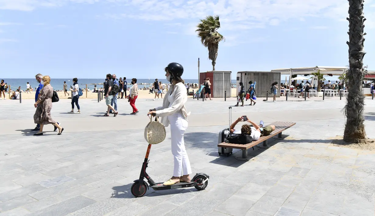 Seorang wanita mengendarai skuter listrik di kawasan pejalan kaki di Pantai Bogatell di Barcelona, Minggu (6/6/2021). Spanyol mengizinkan semua turis yang sudah divaksinasi corona memasuki negaranya mulai 7 Juni mendatang. (Pau BARRENA/AFP)