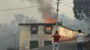 Warga mengambil gambar rumah yang terbakar di Caminho do Meio selama kebakaran hutan yang melanda pulau Madeira di Portugal, Rabu (10/8). Sedikitnya tiga orang tewas dan lebih dari 1.000 orang dievakuasi akibat kebakaran ini. (REUTERS/Duarte Sa)
