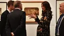 Kate Middleton mengobrol saat melihat pameran fotografi di National Portrait Gallery Exhibition, London, 28 Februari 2018. Kate memperlihatkan tampak samping perutnya yang semakin membesar di usia kehamilannya bulan ke-7. (AP/Frank Augstein)