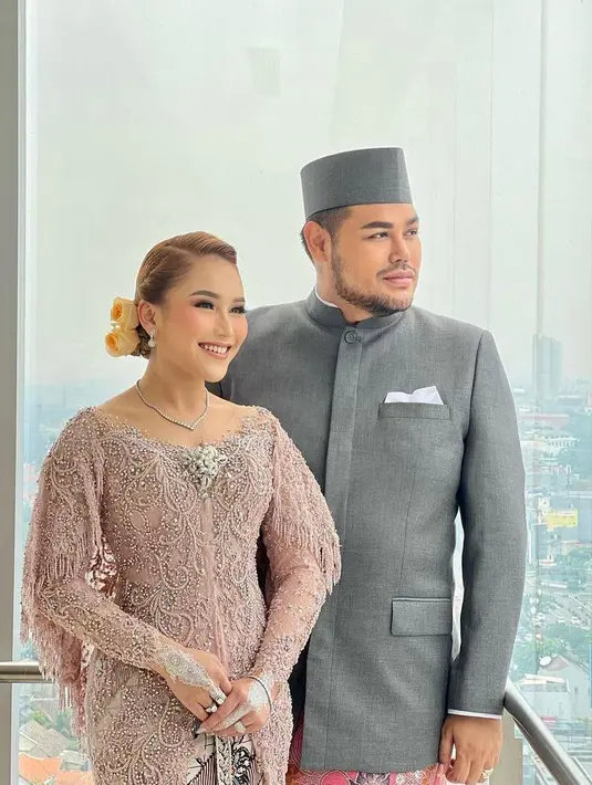 Di momen resepsi, Ayu Ting Ting berganti pakaian menjadi kebaya warna pink berhiaskan payet. Tampilannya tersebut juga serasi dengan Ivan yang mengenakan beskap abu-abu dan kain batik warna pink. (Instagram/ivan_gunawan).