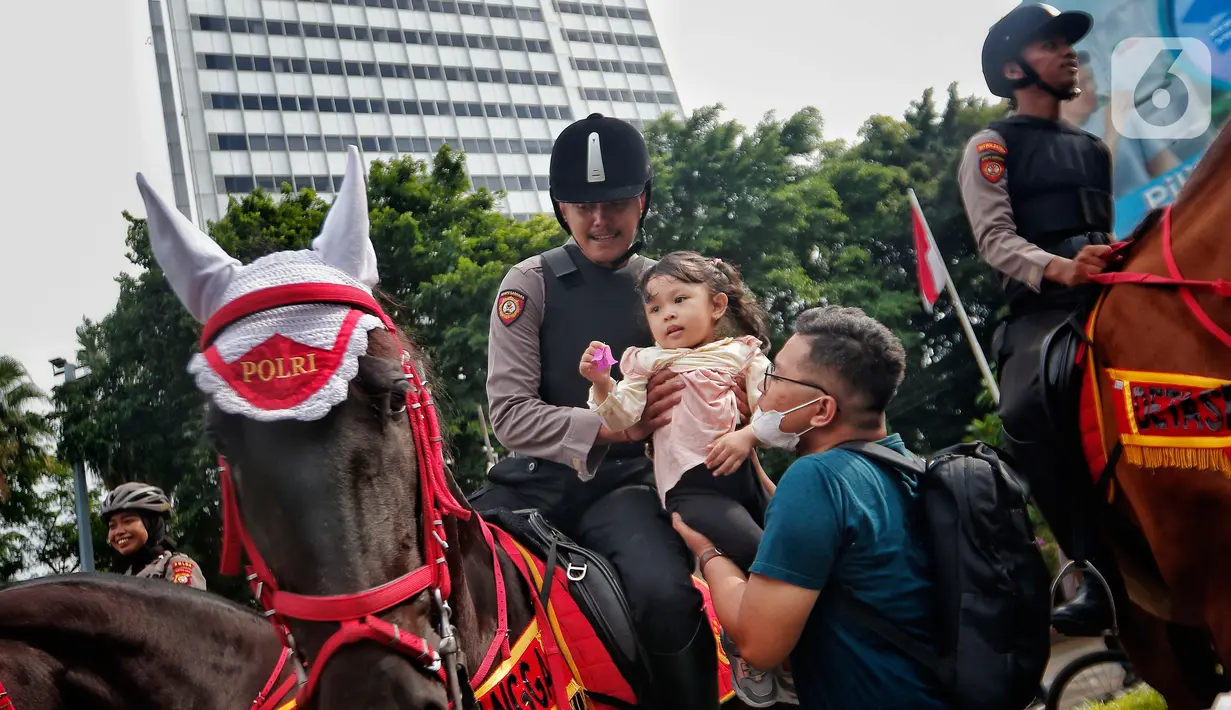Polisi dari Detasemen Turangga Direktorat Polisi Satwa Polri menaiki seorang anak ke atas kuda saat Car Free Day (CFD) atau Hari Bebas Kendaraan Bermotor di kawasan Bundaran HI, Jakarta, Minggu (19/2/2023).Polisi berkuda selain ditugaskan untuk pengamanan simpatik juga untuk menghibur warga dan anak-anak saat Hari Bebas Kendaraan Bermotor serta memperkenalkan profesi tersebut kepada warga. (Lipitan6.com/Angga Yuniar)