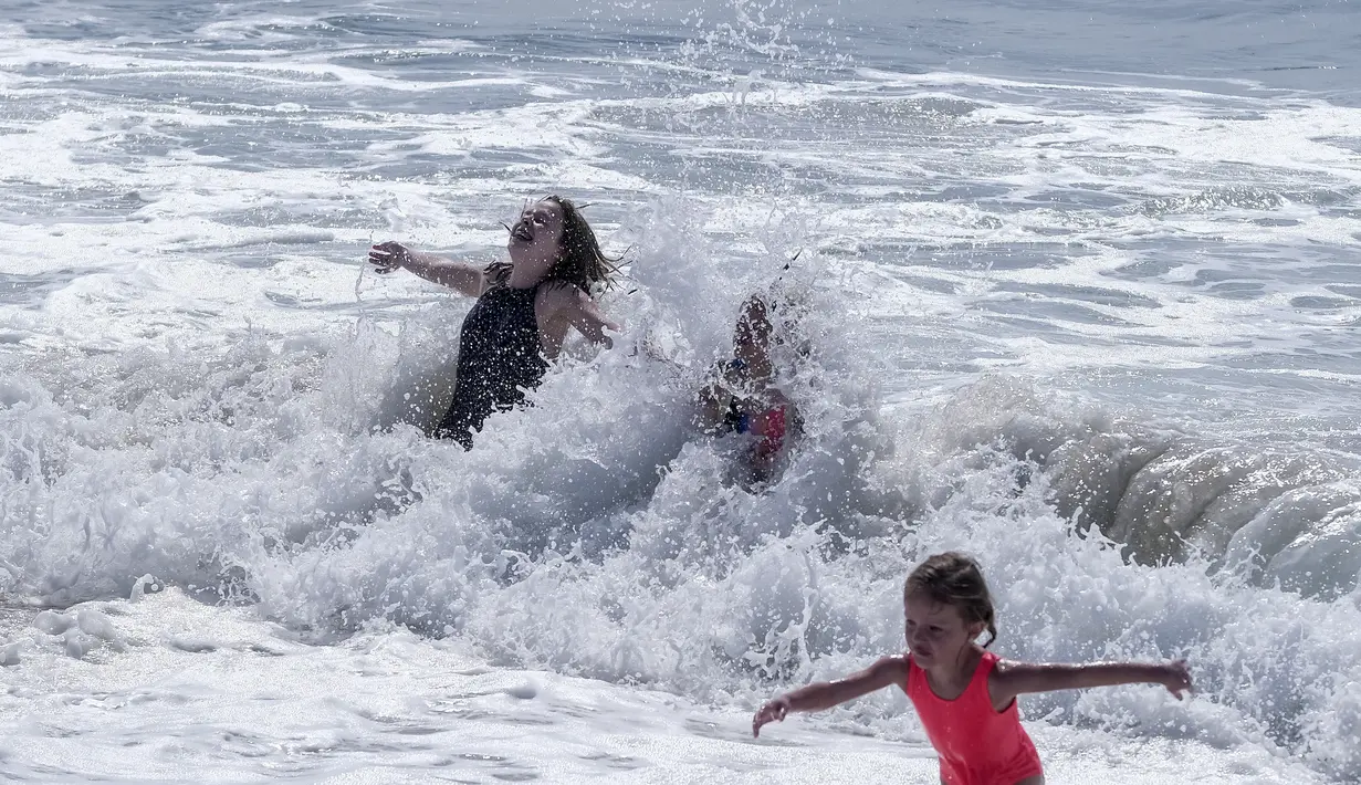 Pengunjung pantai bermain di air di Pantai Huntington, California, Senin (11/10/2021). Pantai Huntington membuka kembali garis pantainya setelah hasil pengujian air kembali dengan jumlah racun terkait minyak yang tidak terdeteksi di air laut. (AP Photo / Ringo HW Chiu)