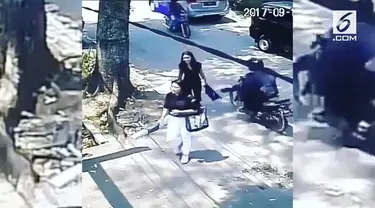 Seorang wanita yang sedang berjalan kaki dijambret oleh seorang pengendara motor. Kejadian ini terekam CCTV sebuah gedung.