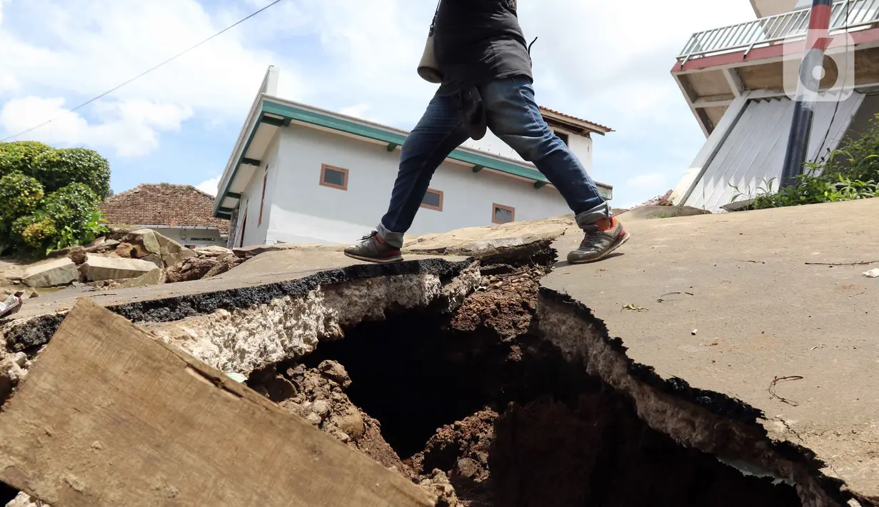 Warga berjalan melintasi jalan yang rusak akibat gempa di Desa Sarampad, Kabupaten Cianjur, Jawa Barat, Selasa (22/11/2022). Gempa dengan magnitudo 5,6 mengakibatkan sejumlah rumah dan jalan di Desa Sarampad rusak parah. (Liputan6.com/Herman Zakharia)
