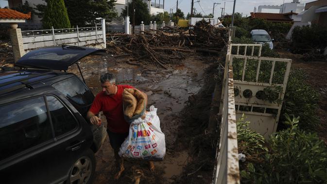 Seorang pria membawa barang miliknya dari rumahnya yang rusak ke mobilnya setelah badai di desa Kineta, Athena (25/11/2019). Pihak berwenang di Yunani mengatakan dua orang telah tewas dan ratusan lainnya luka-luka. (AP Photo/Petros Giannakouris)