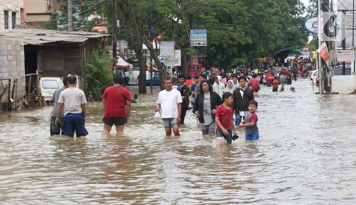 Warga melintasi banjir yang menggenangi Jalan KH Hasyim Ashari, Tangerang, Banten, Kamis (2/1/2020). Banjir yang menggenangi jalan penghubung Jakarta- Tangerang tersebut mulai surut dan sudah bisa dilintasi pejalan kaki. (Liputan6.com/Angga Yuniar)