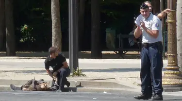 Polisi militer Prancis berlutut dekat jasad seorang pria usai serangan terhadap van polisi di jalan Champs Elysees, Paris, Senin (19/6). Pelaku menggunakan mobil sedan putih untuk menabrakkan diri ke van polisi di jalanan kota. (Noemie Pfister via AP)