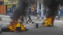 Seorang pria menambahkan puing-puing untuk dibakar di barikade ban yang terbakar yang dipasang oleh pengunjuk rasa selama demonstrasi menuntut Perdana Menteri Haiti Ariel Henry mundur dan menyerukan kualitas hidup yang lebih baik, di Port-au-Prince, Haiti, Senin (29/8/2022). (AP Photo/Odelyn Joseph)