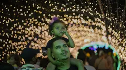 Seorang pria menggendong putrinya saat acara lampu Natal di taman Ibirapuera di Sao Paulo, Brasil, Selasa (14/12/2021). Jelang perayaan Natal, taman dan pantai dihiasi lampu-lampu yang indah. (AP Photo/Andre Penner)