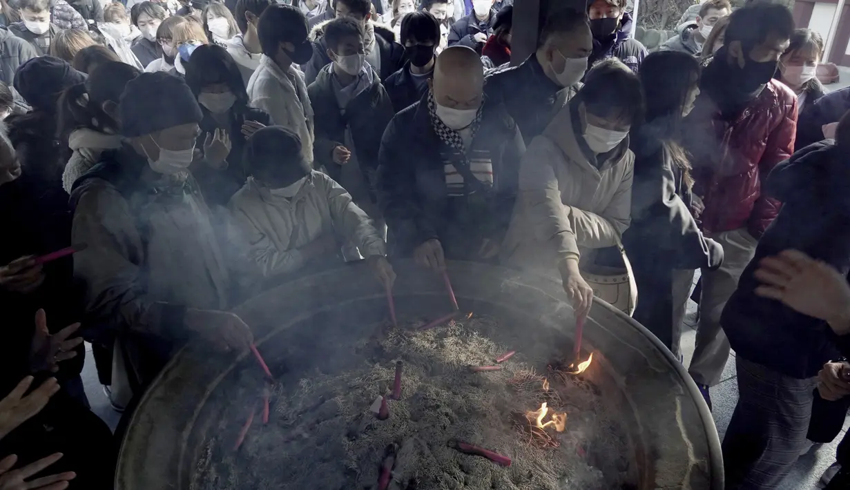 Pengunjung membakar joss stick untuk keberuntungan selama "hatsumode", atau kunjungan pertama mereka tahun ini ke kuil atau kuil, di kuil Kawasaki Daishi di Kawasaki, dekat Tokyo, Senin (3/1/2022). (AP Photo/Eugene Hoshiko)