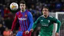 Bek Barcelona, Gerard Pique berebut bola dengan pemain Osasuna, Kike Garcia selama pertandingan lanjutan La Liga Spanyol di di stadion Camp Nou di Barcelona, Senin (14/3/2022). Barcelona menang telak atas Osasuna 4-0. (AFP/Josep Lago)