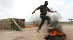Seorang pejuang Jaysh al-Izza (the Army of Glory) melompati api saat melakukan latihan di kota Idlib, Suriah (9/4). Pejuang Jaysh al-Izza ini adalah afiliasi dari tentara Suriah yang didukung oleh Turki. (AFP/Omar Haj Kadour)