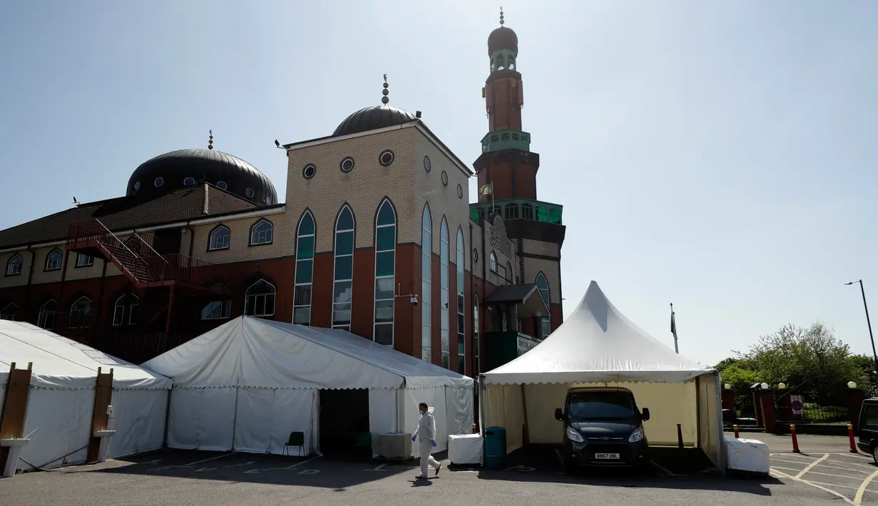 Sukarelawan berpakaian pelindung berjalan di halaman parkir Central Jamis Mosque Ghamkol Sharif di Birmingham, Inggris pada 24 April 2020. Saat masjid itu tutup selama Ramadan di tengah pandemi, tempat parkirnya digunakan menjadi kamar mayat sementara untuk korban corona Covid-19. (AP/Matt Dunham)