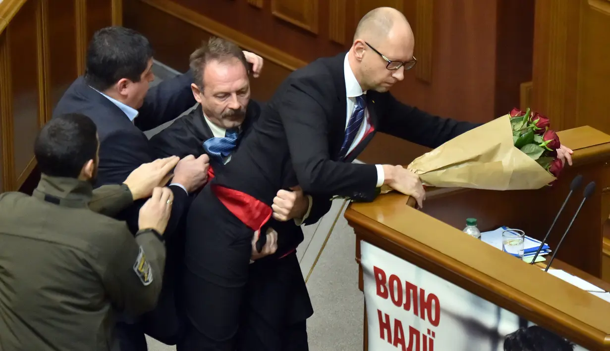 Seorang anggota parlemen bernama Oleg Barna tampak menyeret PM Arseny Yatsenyuk (kanan) dari podium saat membacakan laporan tahunan kinerja Pemerintah Ukraina di Majelis Tinggi Parlemen Ukraina, 11 Desember 2015. (Sergei SUPINSKY/AFP)