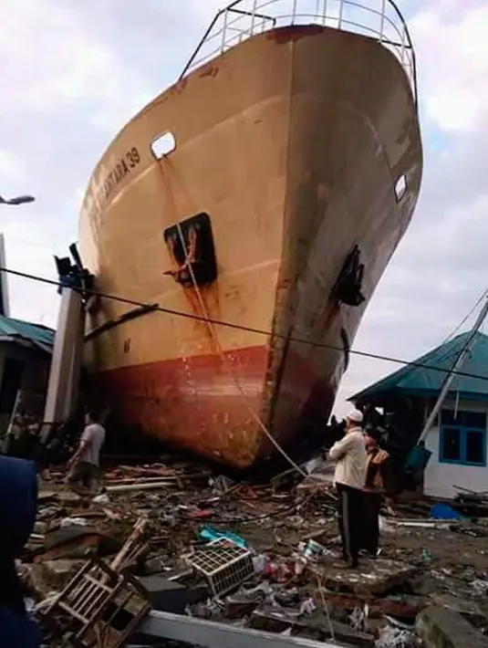 Penduduk desa melihat sebuah kapal yang tersapu hingga ke darat oleh tsunami di Kota Palu di Sulawesi Tengah, Sabtu (29/9). Gelombang tsunami setinggi 3 meter yang menerjang Palu terjadi setelah gempa bumi mengguncang Palu dan Donggala. (AP/Rio Mario)