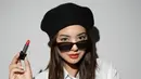 Gaya Parisian chic ala Aurelie Moeremans yang sangat pas dengan parasnya. Ia mengenakan kemeja putih lengan sesiku, topi hitam, sunglasses, dan memulas bibirnya dengan lipstick merah merona. [Foto: Instagram/aurelie]