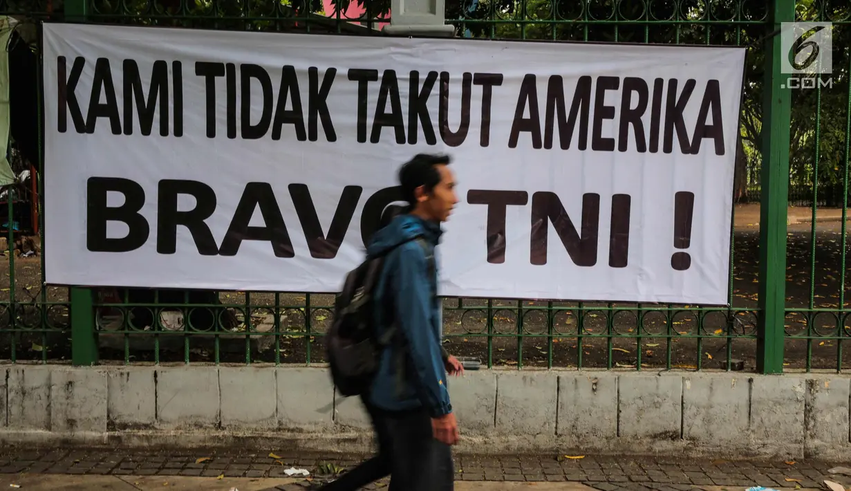 Warga melintas di depan spanduk bertulisan "Kami Tidak Takut Amerika Bravo TNI" terpampang di pagar Stasiun Gambir, Jakarta, Senin (23/10). Pemasangan spanduk ini diduga terkait undangan Panglima TNI yang ditolak masuk AS. (Liputan6.com/Faizal Fanani)