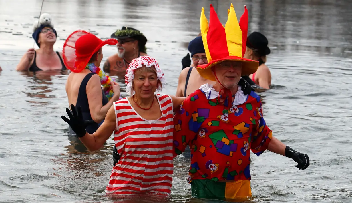 Anggota klub renang es "Berliner Seehunde" merayakan tahun baru dengan berenang di danau Orankesee, Berlin, Jerman (1/1). Diantara mereka ada anggota yang mengenakan pakaian bertema badut. (REUTERS/Fabrizio Bensch)