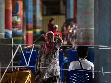 Seorang warga menunjukan jarinya usai menggunakan hak pilihnya dalam Pilkada DKI Jakarta dengan melakukan pencoblosan di TPS 21 di bawah kolong jembatan tol akses Bandara, Petak Asem, Jakarta, Rabu (15/2). (Liputan6.com/Faizal Fanani)